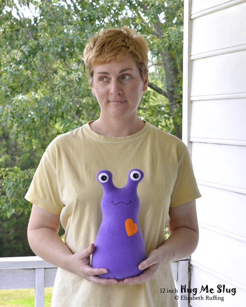 Purple fleece Hug Me Slug, with an orange heart, original art toy by Elizabeth Ruffing, also pictured