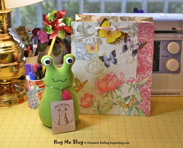 Grass green Hug Me Slug stuffed animal art toy by artist Elizabeth Ruffing with pink butterfly gift bag and personalized hang tag