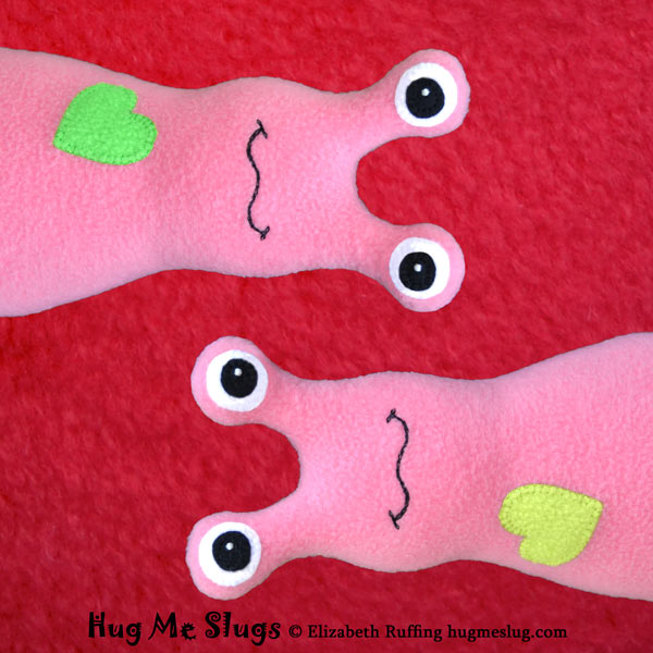 Hug Me Slugs equality symbol, pink fleece banana slug stuffed animal toys on a red background by artist Elizabeth Ruffing