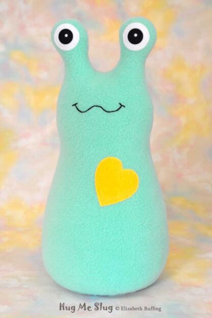 A smiling aqua fleece stuffed animal slug with a yellow heart
