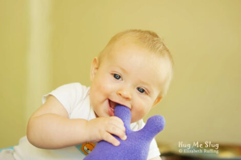 Baby chewing on his purple fleece Hug Me Slug plush toy