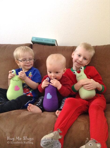 Three brothers with their pear green and purple fleece Hug Me Slug plush toys