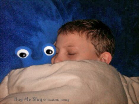 Royal blue fleece Hug Me Slug plush toy under covers with sleeping boy