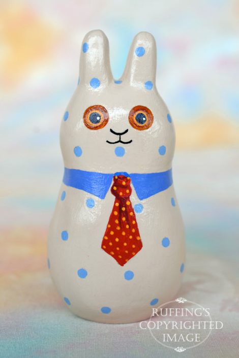 A tan bunny figurine with blue polka dots, a blue collar, and a red tie with yellow polka dots.