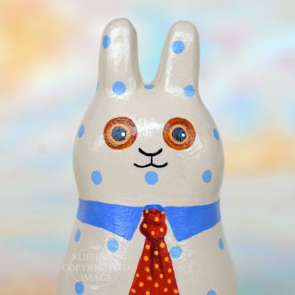 A tan bunny figurine with blue polka dots, a blue collar, and a red tie with yellow polka dots.