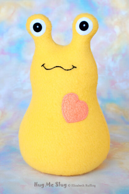 A smiling yellow stuffed animal slug with a soft orange heart
