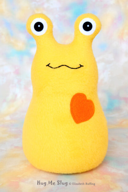 A smiling yellow stuffed animal slug with an orange heart