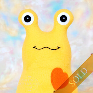 Smiling yellow fleece slug with an orange heart marked sold