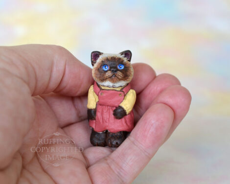 Miniature Himalayan kitten figurine in a mauve pinafore with a painted gold blouse, sitting in a hand