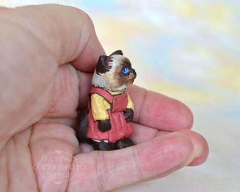 Miniature Himalayan kitten figurine in a mauve pinafore with a painted gold blouse, sitting in a hand