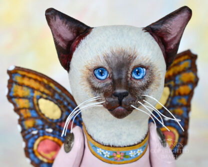 A Siamese cat art doll with bright blue eyes and multicolored wings.