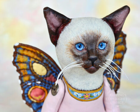 A Siamese cat art doll with bright blue eyes and multicolored wings.