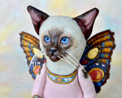 A Siamese cat art doll with bright blue eyes and multicolored wings.