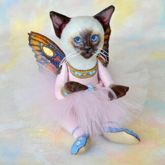 A Siamese cat art doll with bright blue eyes, a lavender-pink tutu, and multicolored wings sits on a soft rainbow colored background.