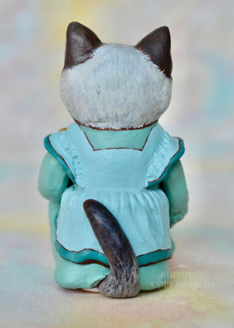 A Ragdoll cat in a light turquoise pinafore, back view with her tail showing