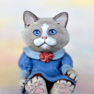 A bi-color ragdoll kitten in a blue dress with a light blue collar and a mauve rose in the middle of her neckline