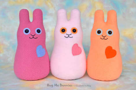 Magenta, light pink, and soft light orange stuffed fleece rabbits, smiling