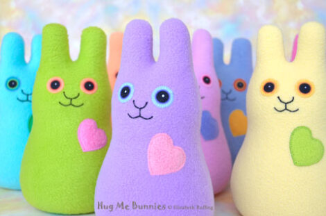 Turquoise, apple green, lavender, pink, blue, and light yellow stuffed fleece rabbits, all smiling