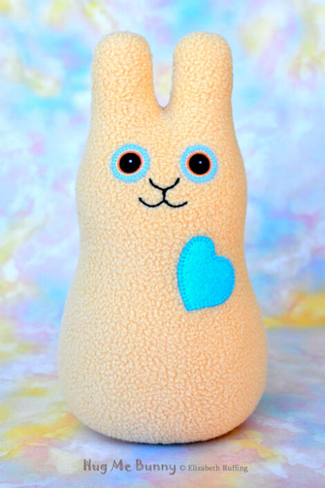 Smiling light camel fleece bunny with a light turquoise heart