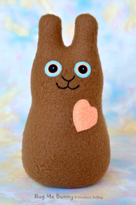 Coffee brown stuffed fleece rabbit with a soft light orange heart and blue eyes, smiles.