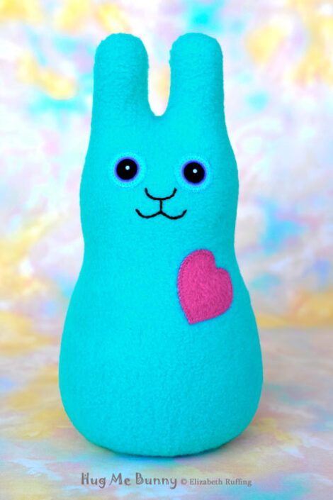 Smiling turquoise blue fleece bunny with a magenta pink heart.