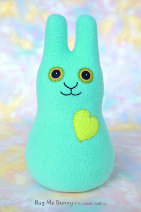 A smiling light aqua green fleece bunny with an apple green heart.