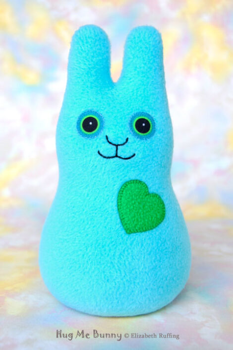 A smiling light turquoise fleece bunny with a Kelly green heart.
