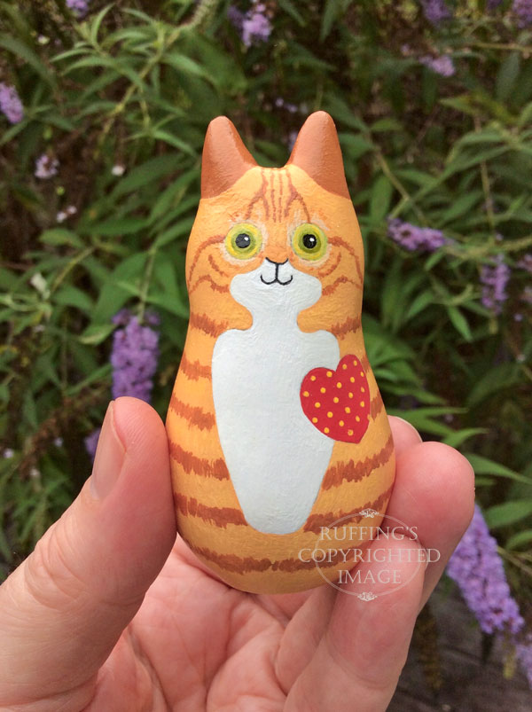 Ginger-and white-tabby cat figurine held by fingertips