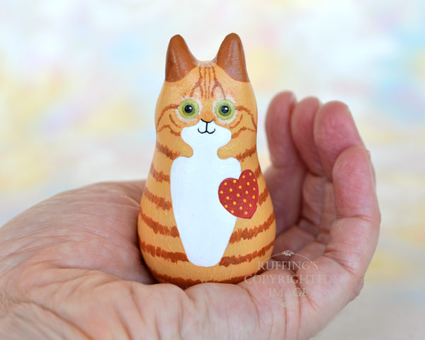 Ginger-and white-tabby cat figurine held in the palm of a hand